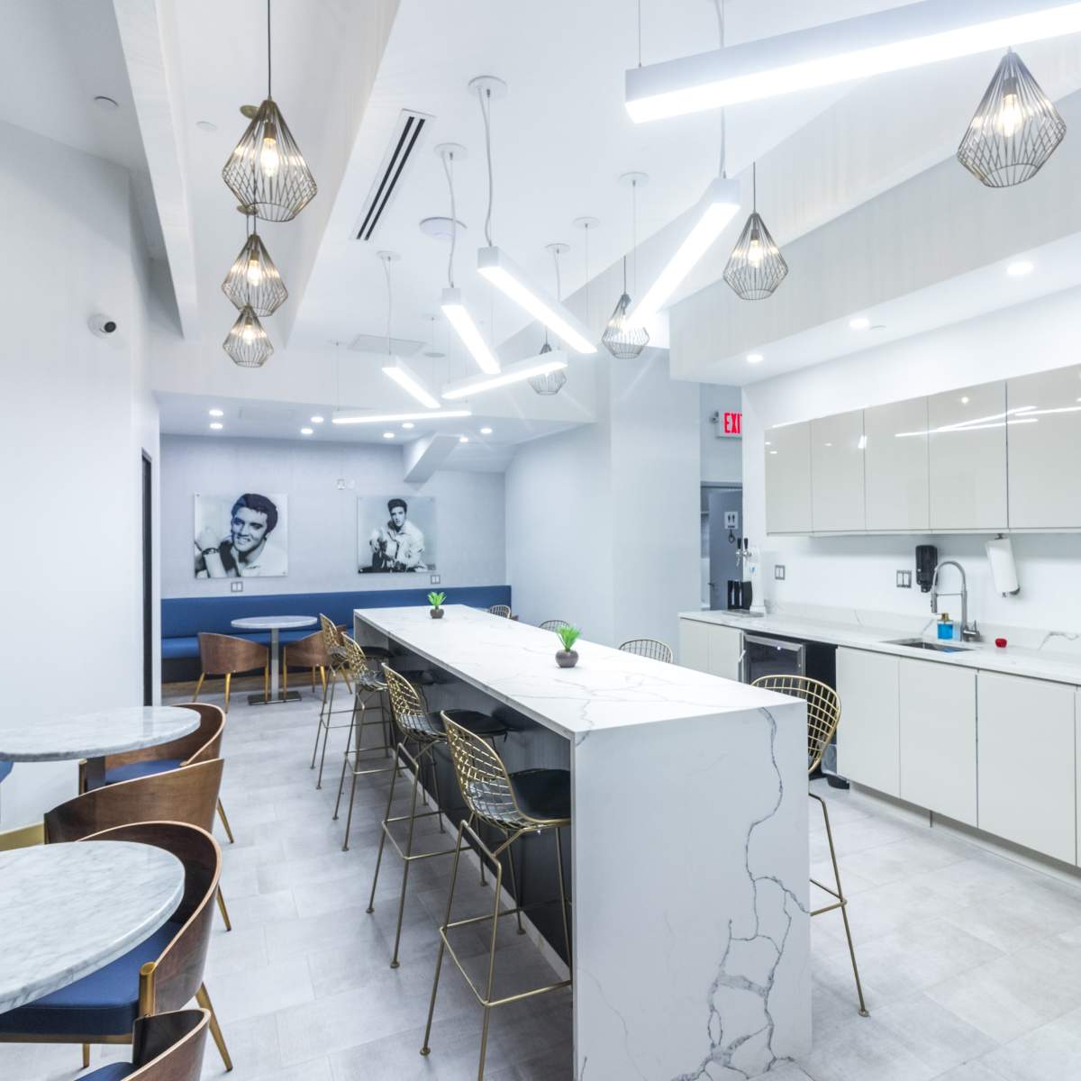 A modern kitchen and dining area features a white countertop, metal chairs, and pendant lighting.
