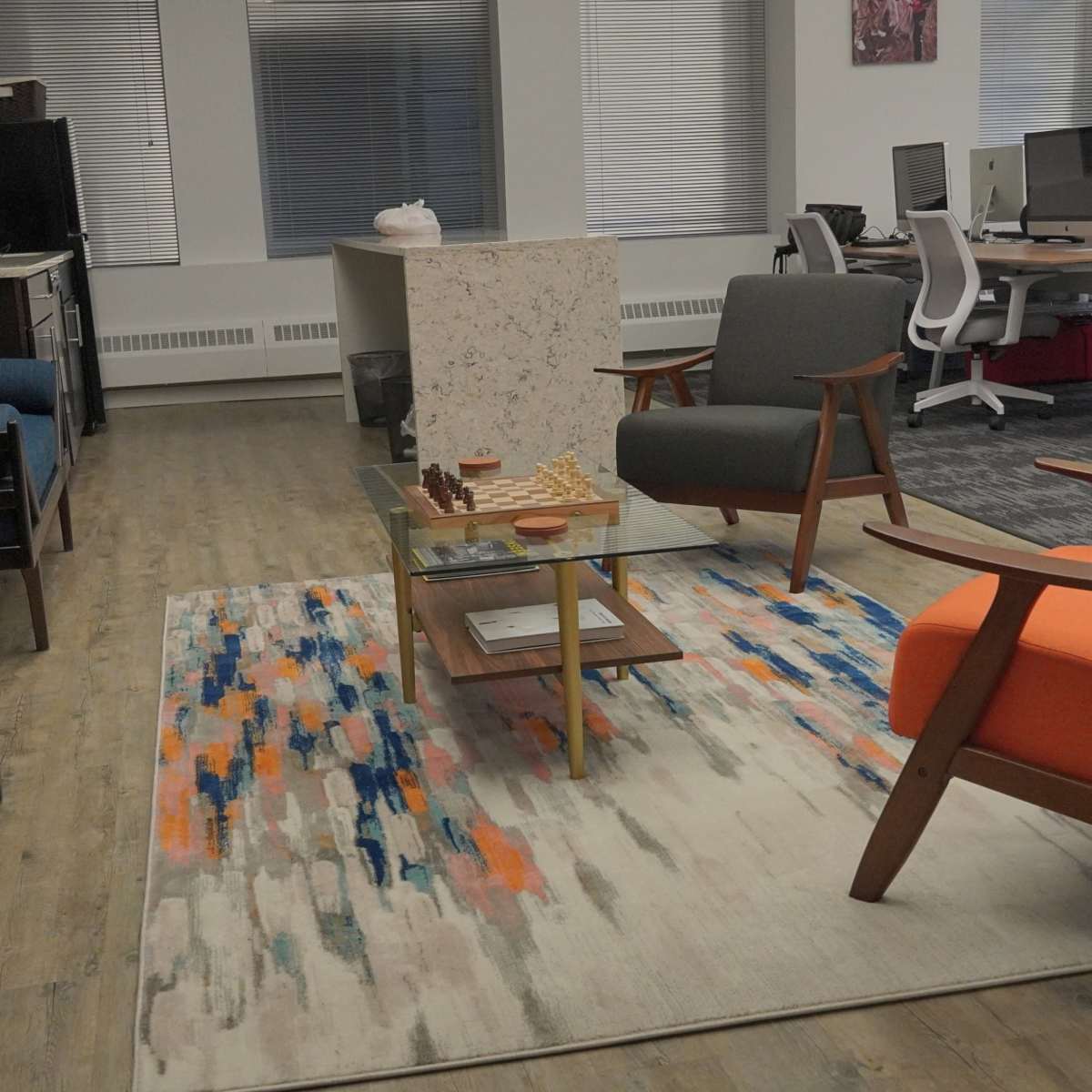 A modern office space with seating areas, a coffee table with a chess set, and workstations in the background.
