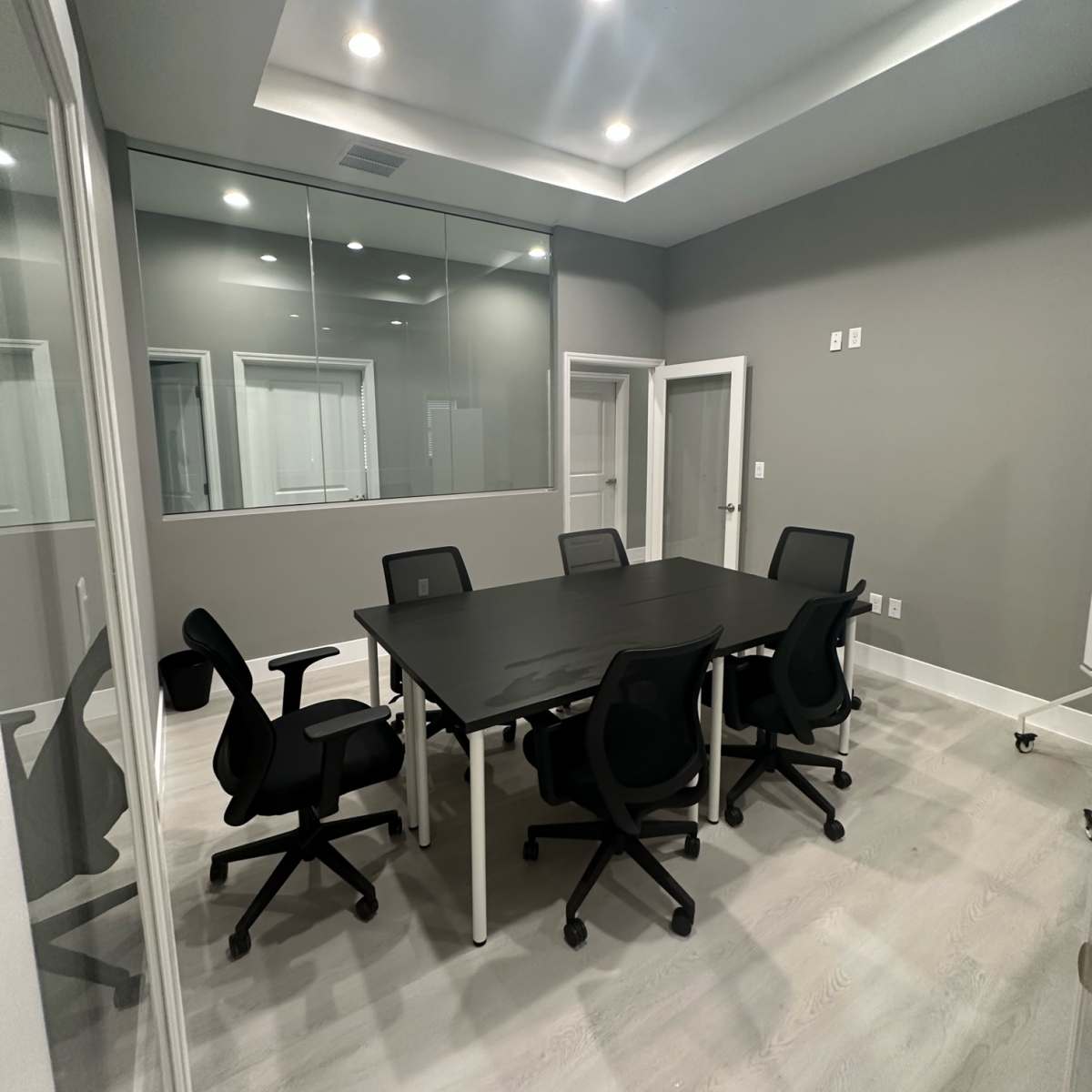 A modern conference room featuring a large black table surrounded by six black chairs, with glass walls and ample lighting.