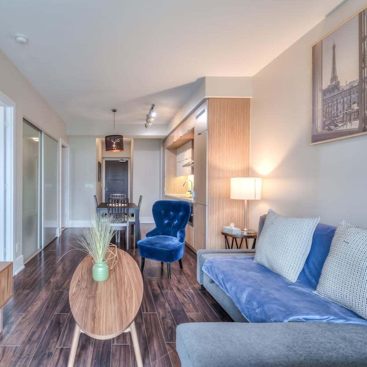 A modern living room features a blue velvet chair, a gray sofa, a wooden coffee table, and a television displaying streaming selections.
