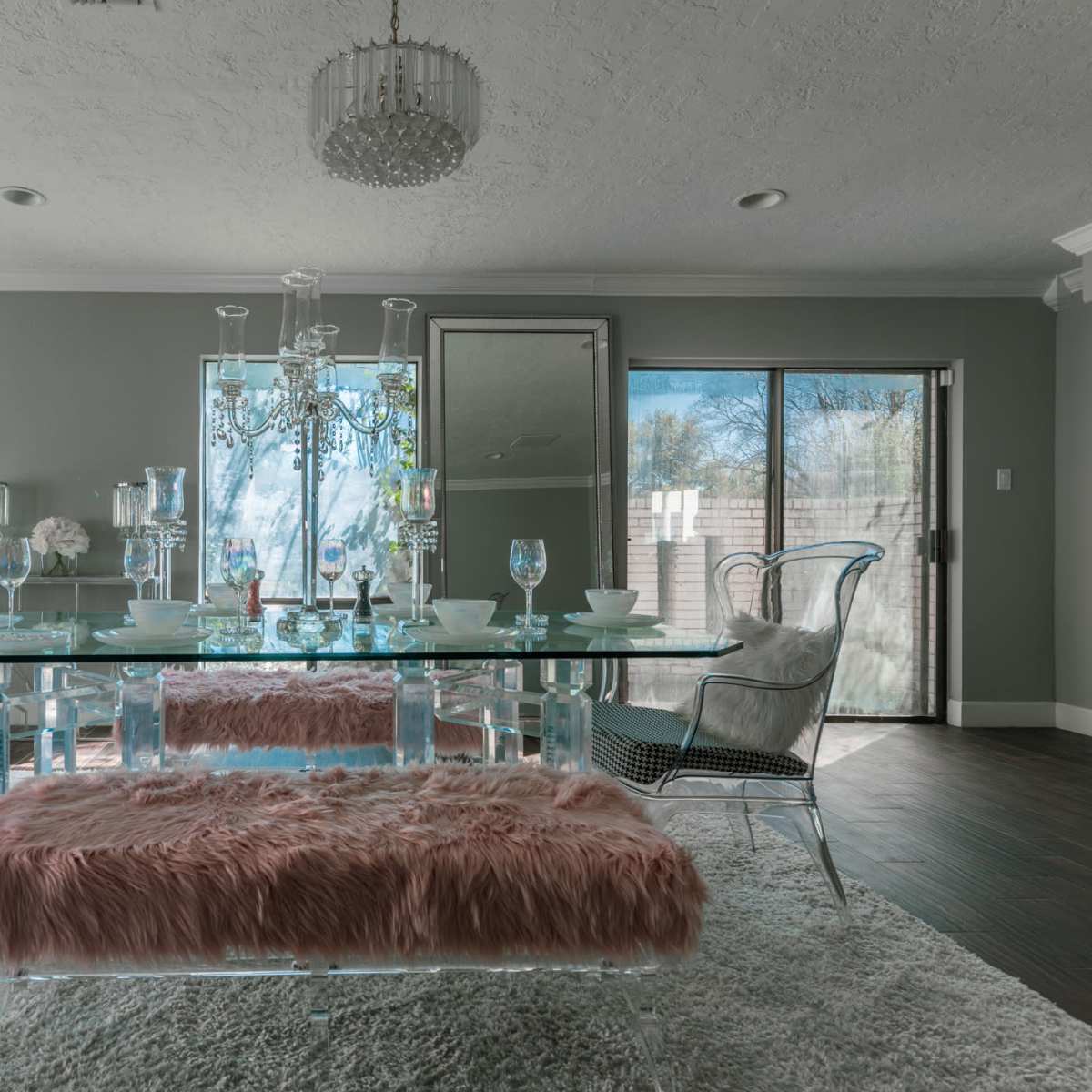 A dining area features a glass table, stylish chairs, and a plush bench on a textured rug, with large windows allowing natural light to illuminate the space.