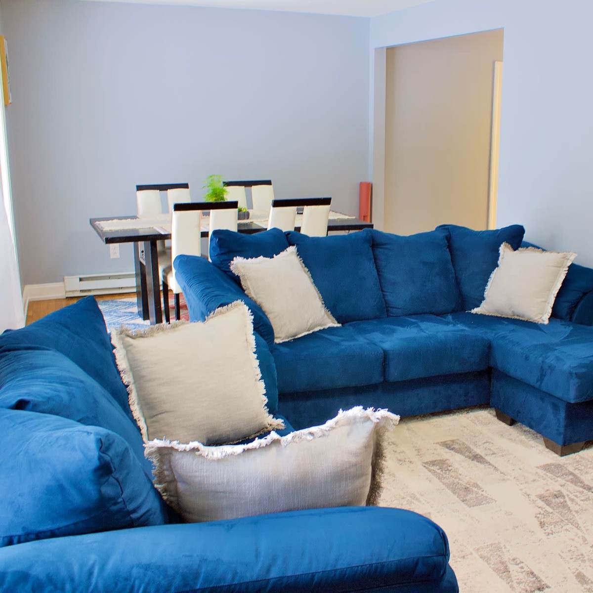 A living room featuring a blue sectional sofa, a black coffee table, and a dining area with a table and chairs in the background.