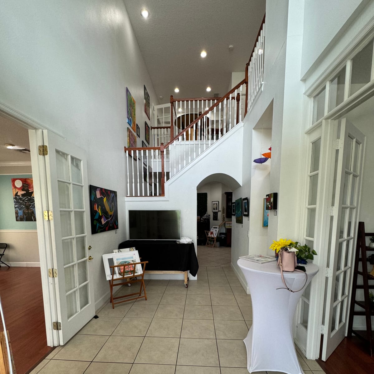 A spacious entryway with a staircase, a small table with a black cloth, and several artworks displayed on the walls.