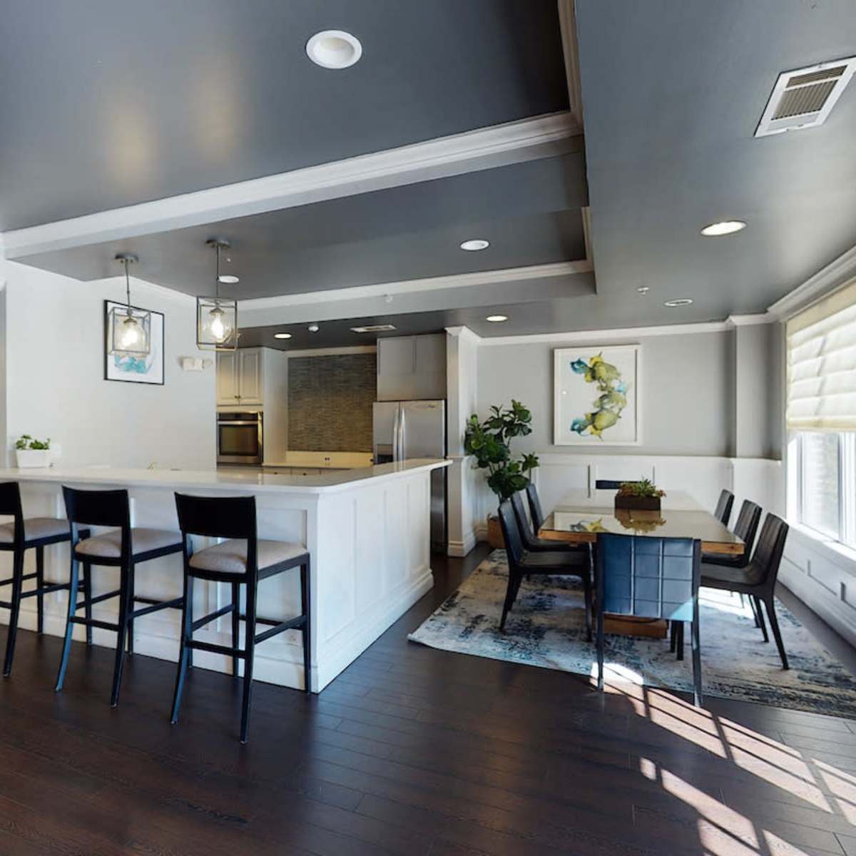 A modern kitchen and dining area with a bar, table, and dark wood flooring.