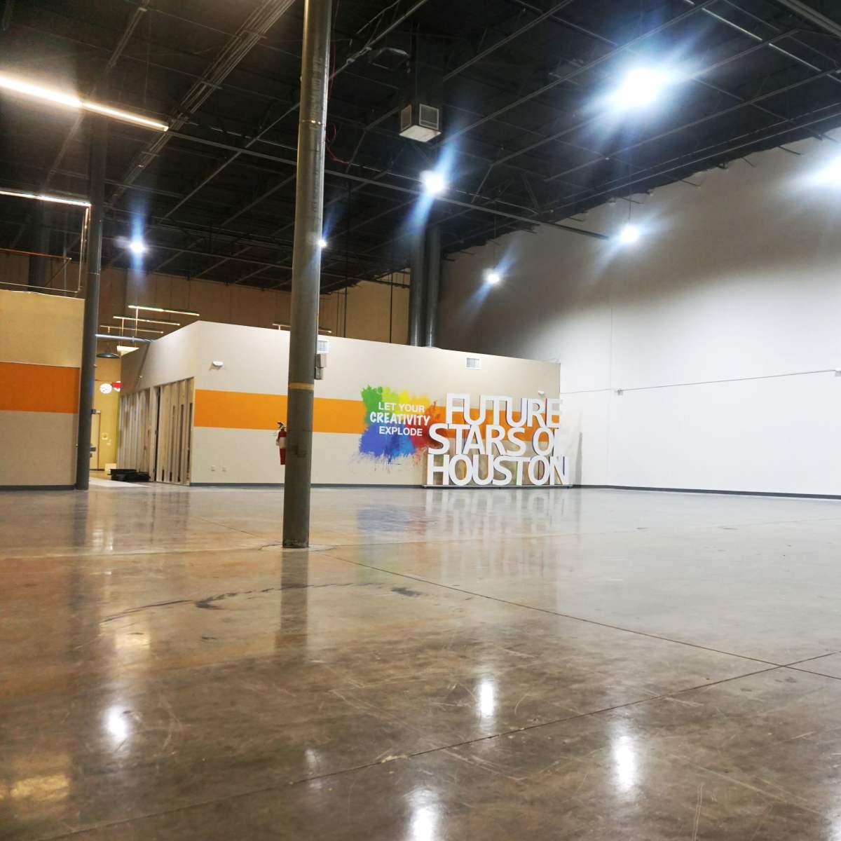 An empty room with polished concrete floors and a large wall featuring the text "FUTURE STARS OF HOUSTON."