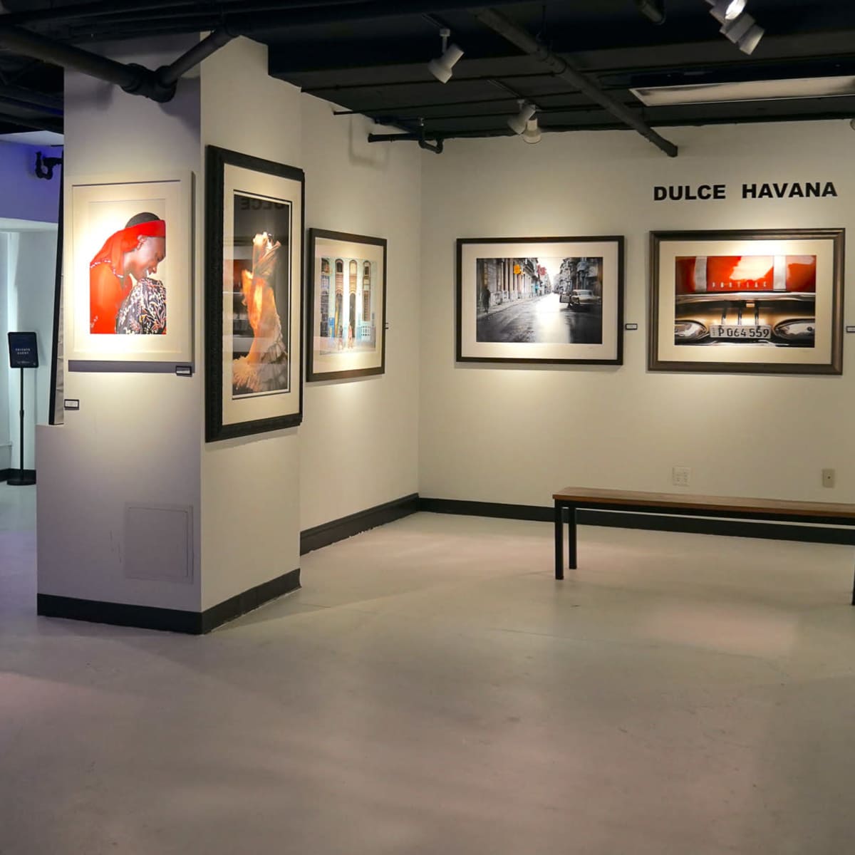 An art gallery with photographs displayed on the walls, a bench in the center, and a merchandise section featuring clothing in the background.