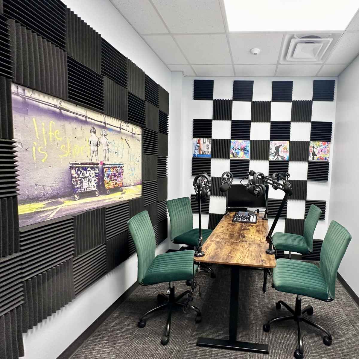 A small recording studio features a wooden table with microphones, surrounded by green chairs and decorated with vibrant wall art and acoustic panels.