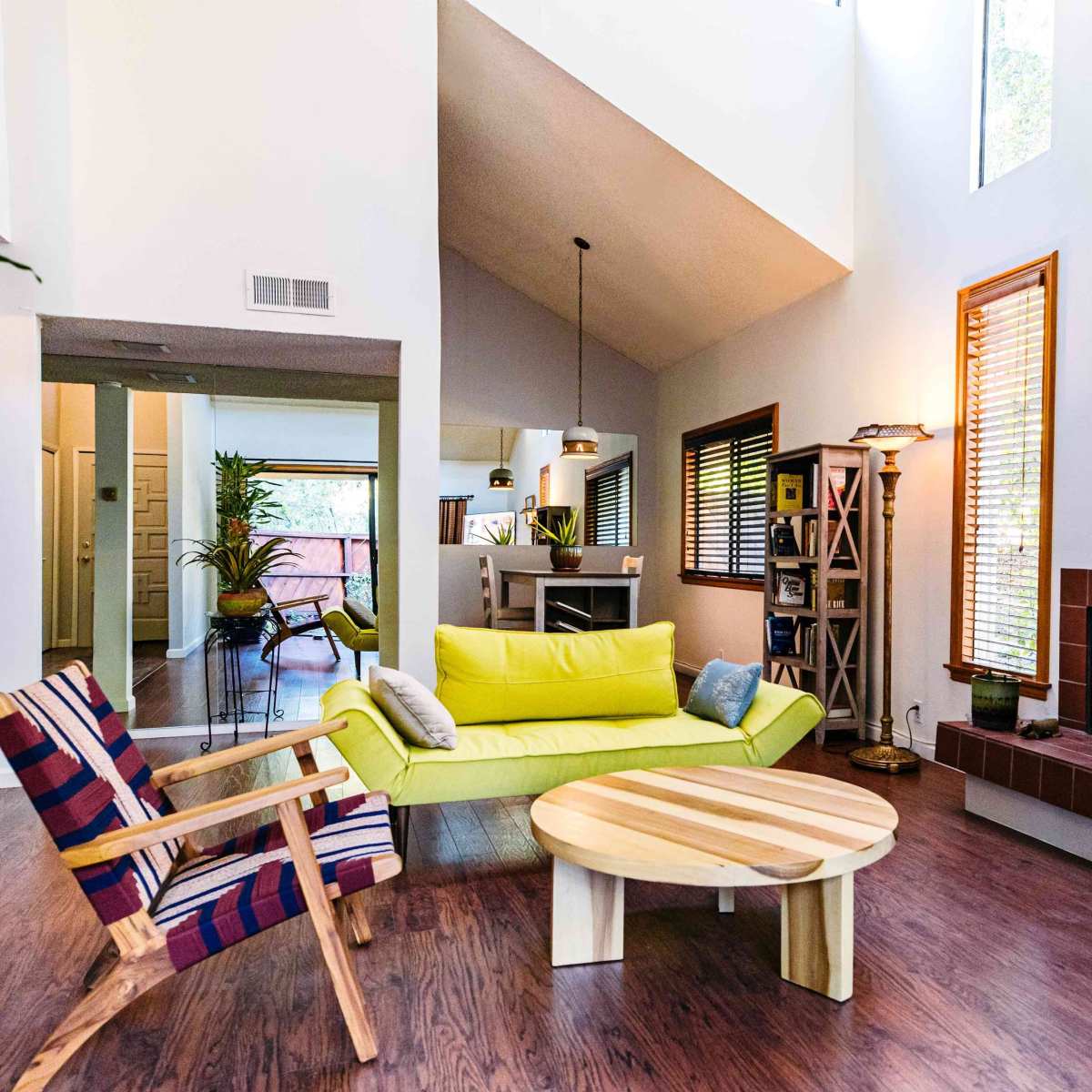 A modern living room features a yellow couch, a round wooden coffee table, and large windows with natural light.