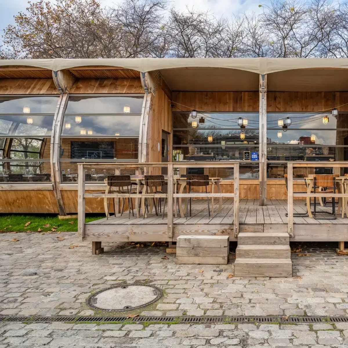 A modern wooden cafe with large glass windows and an outdoor seating area on a stone path.