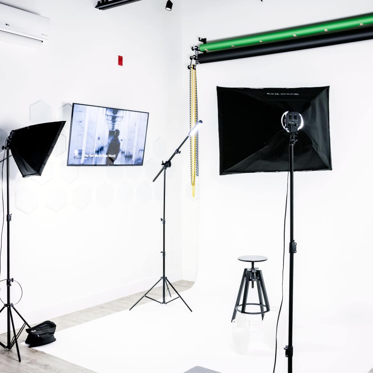 A photography studio setup with a white backdrop, a stool in the center, and various lighting equipment including softboxes and a monitor displaying an image.