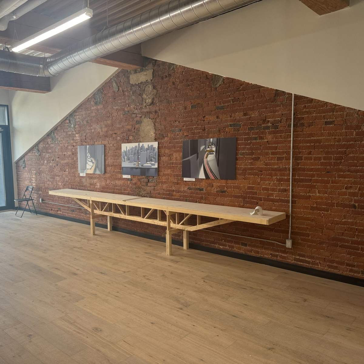 A spacious room with a wooden table along a brick wall, featuring two framed pictures, and large windows allowing natural light to enter.