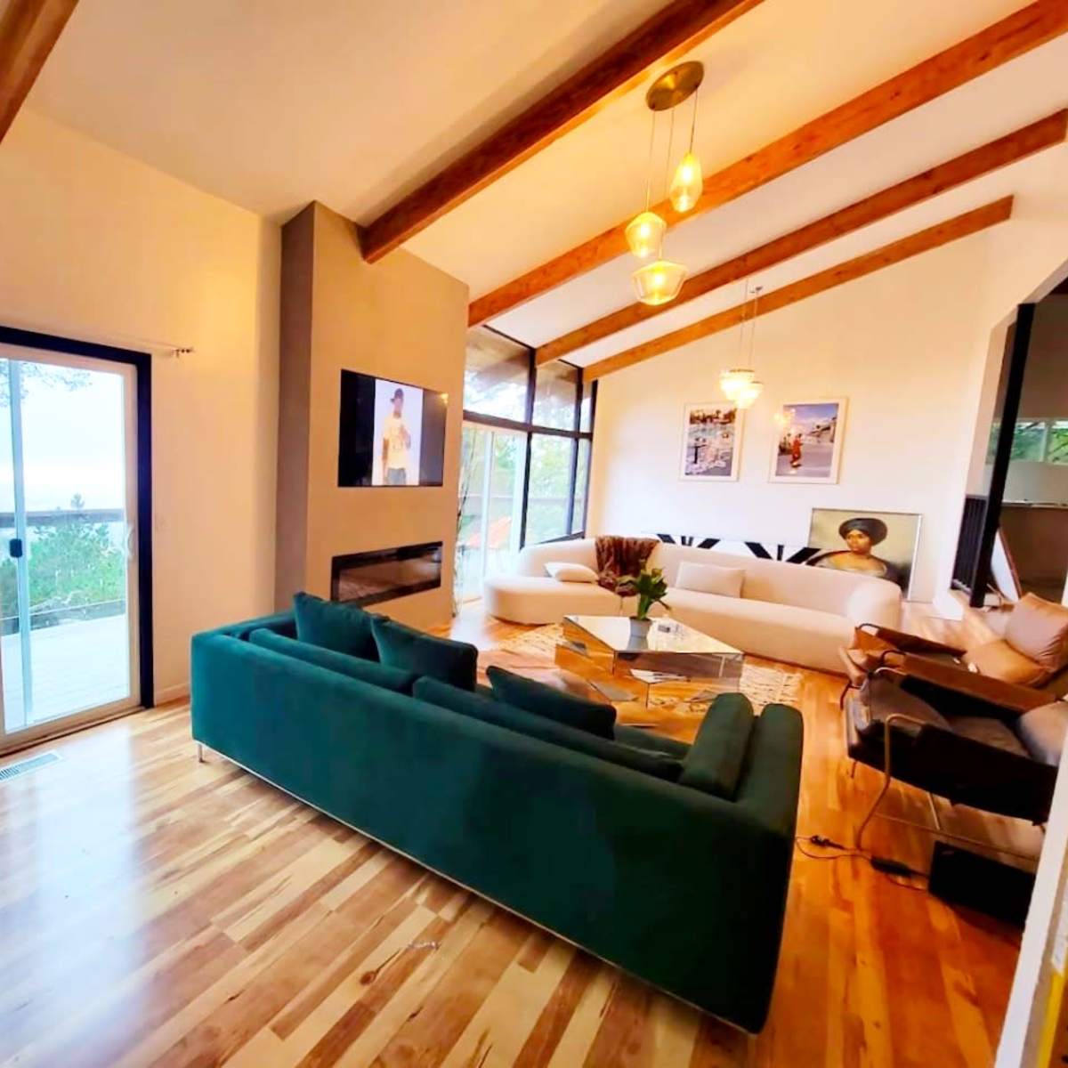 A spacious living room with a green sofa, wooden beams on the ceiling, and large windows that open to a view.