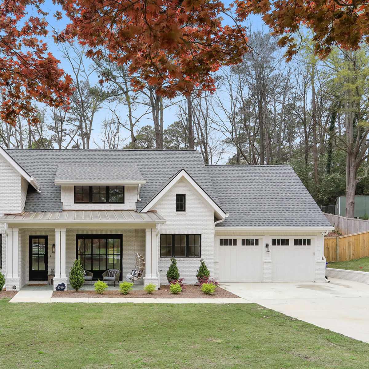 A white brick house with a gray roof, large windows, and a manicured lawn surrounded by trees.