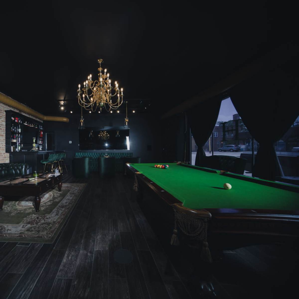 The room features a green billiard table, a vintage-style couch, a chandelier, and a large painting on the wall, creating a lounge atmosphere.