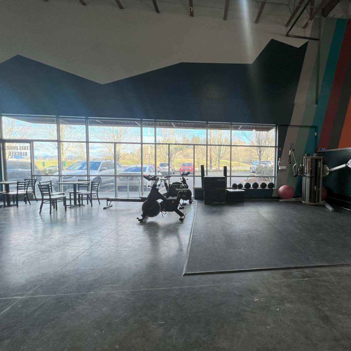 An indoor gym with exercise equipment, large windows on one side, and a section for weights and fitness mats.