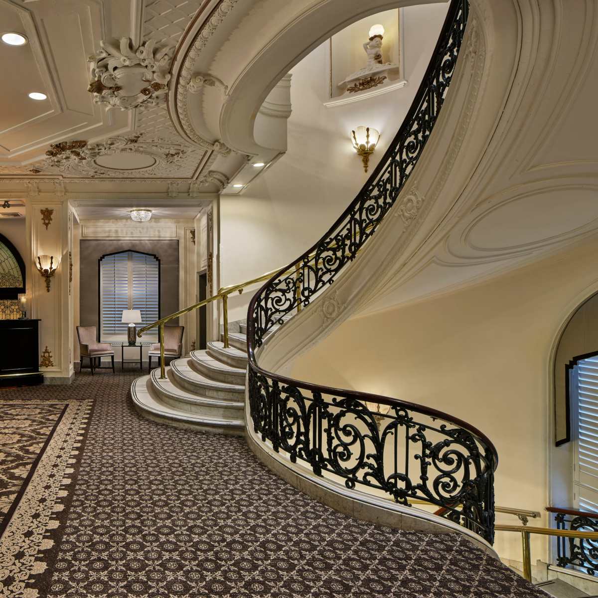 An elegant staircase with ornate railings and decorative ceiling details in a well-lit interior space.