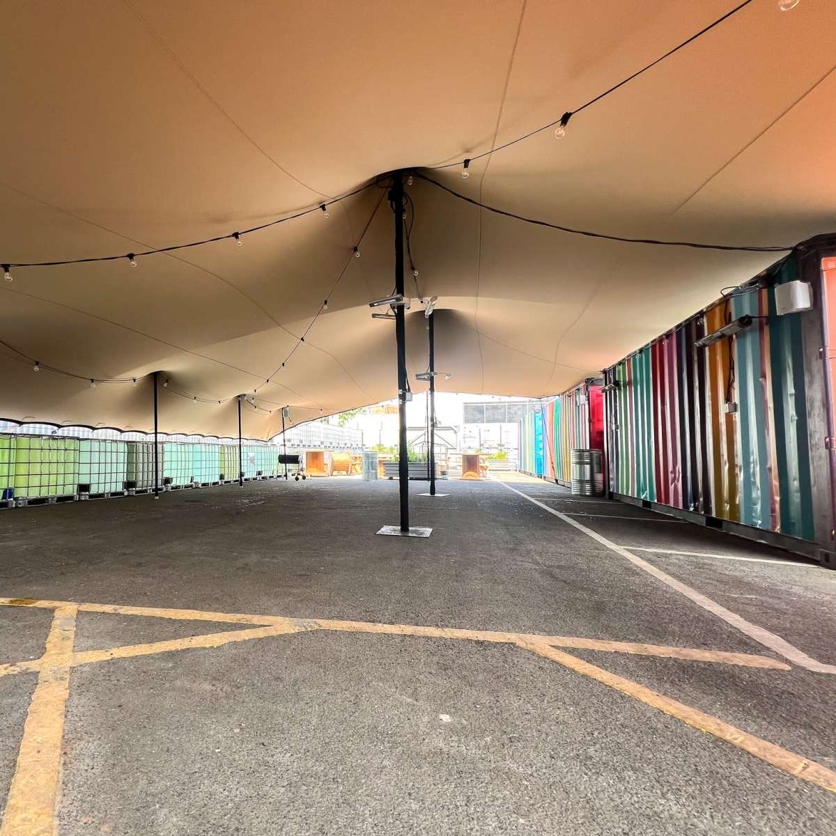 A spacious outdoor area covered by a large tent, with colorful shipping containers lining one side.