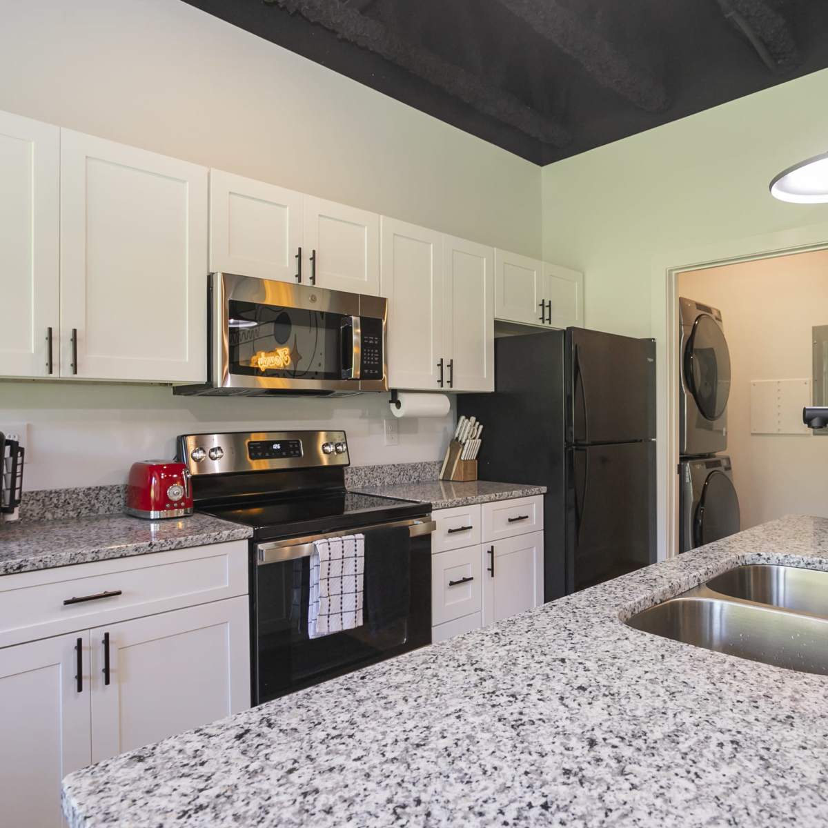 A modern kitchen features white cabinetry, stainless steel appliances, and a granite countertop with a double sink.