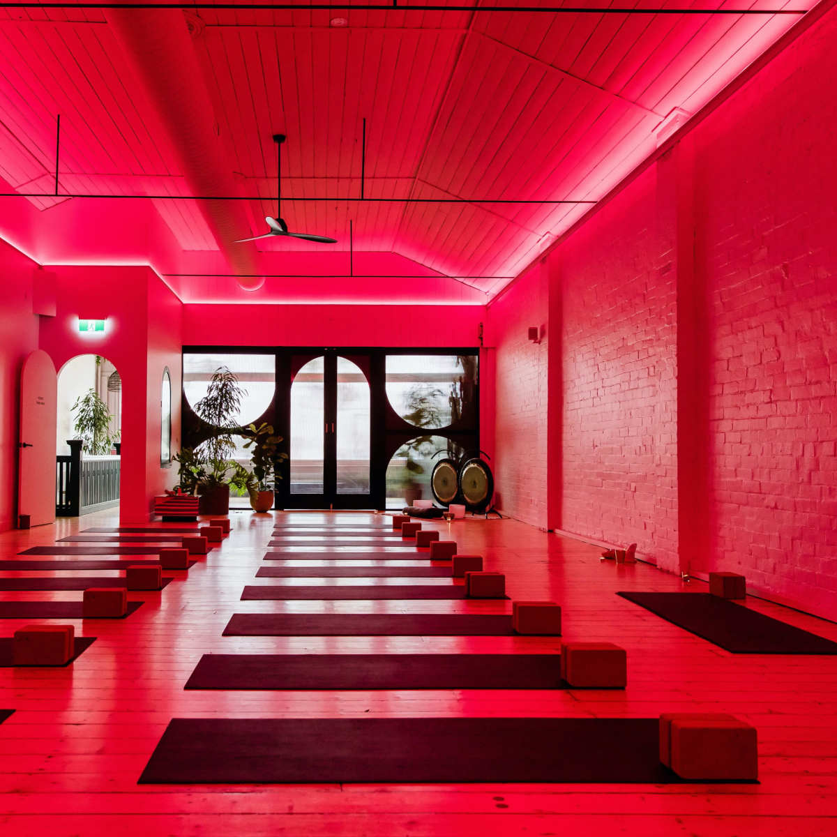 A minimalist yoga studio with rows of mats and props under vibrant pink lighting.