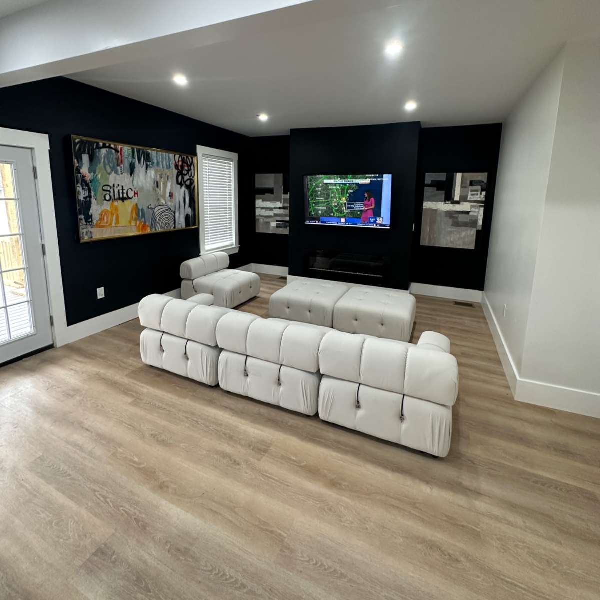A modern living room with a light-colored tufted sofa facing a wall-mounted television and black accent walls.