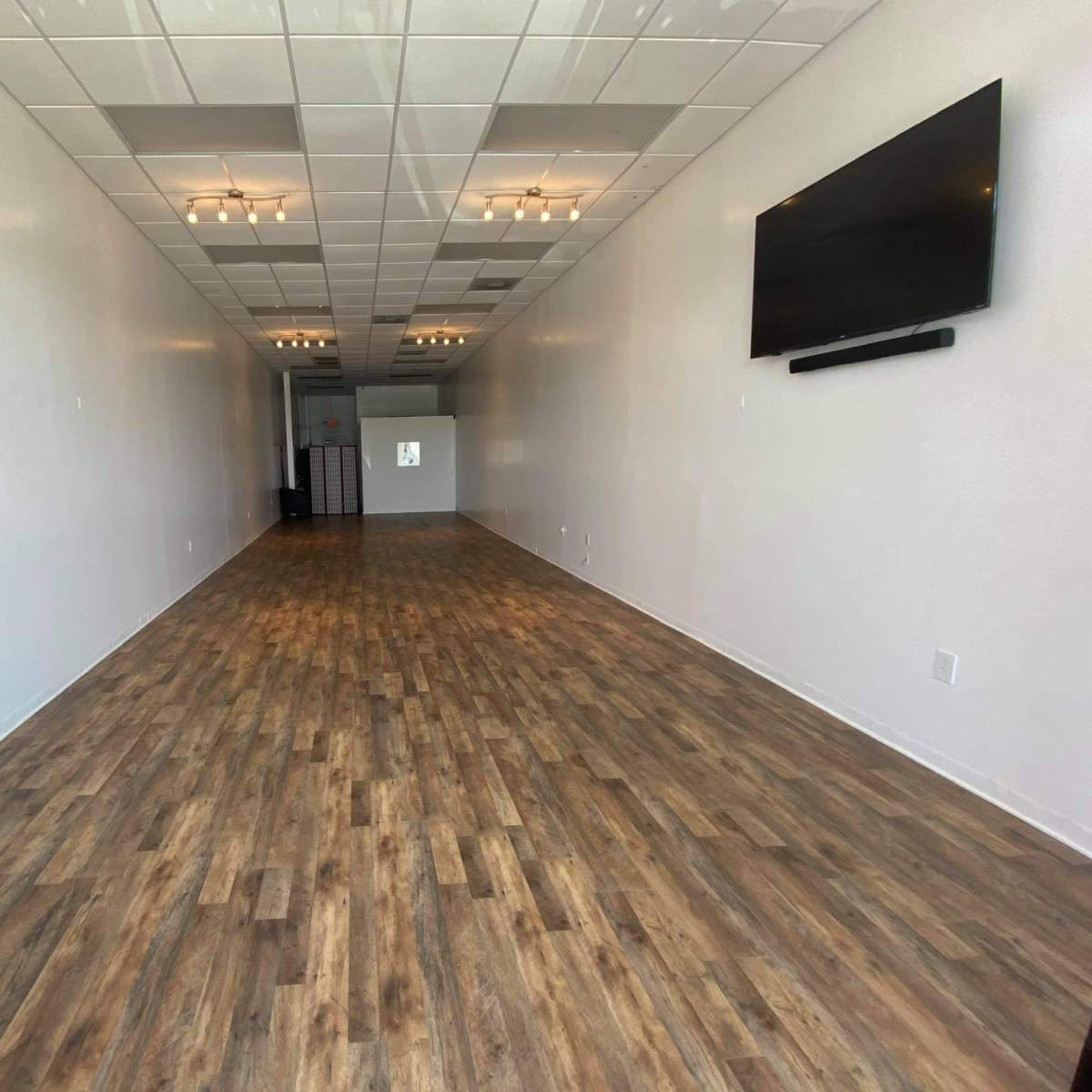 A spacious, empty storefront with wooden flooring and bright overhead lights.