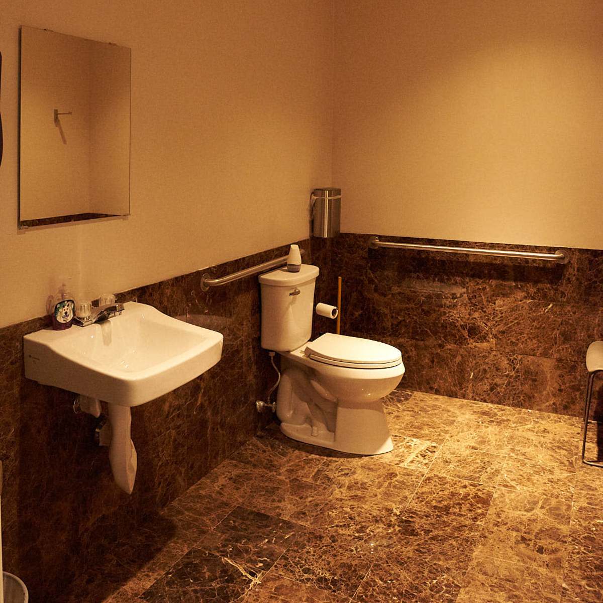 A bathroom with a toilet, a sink mounted on the wall, and marble-patterned flooring.