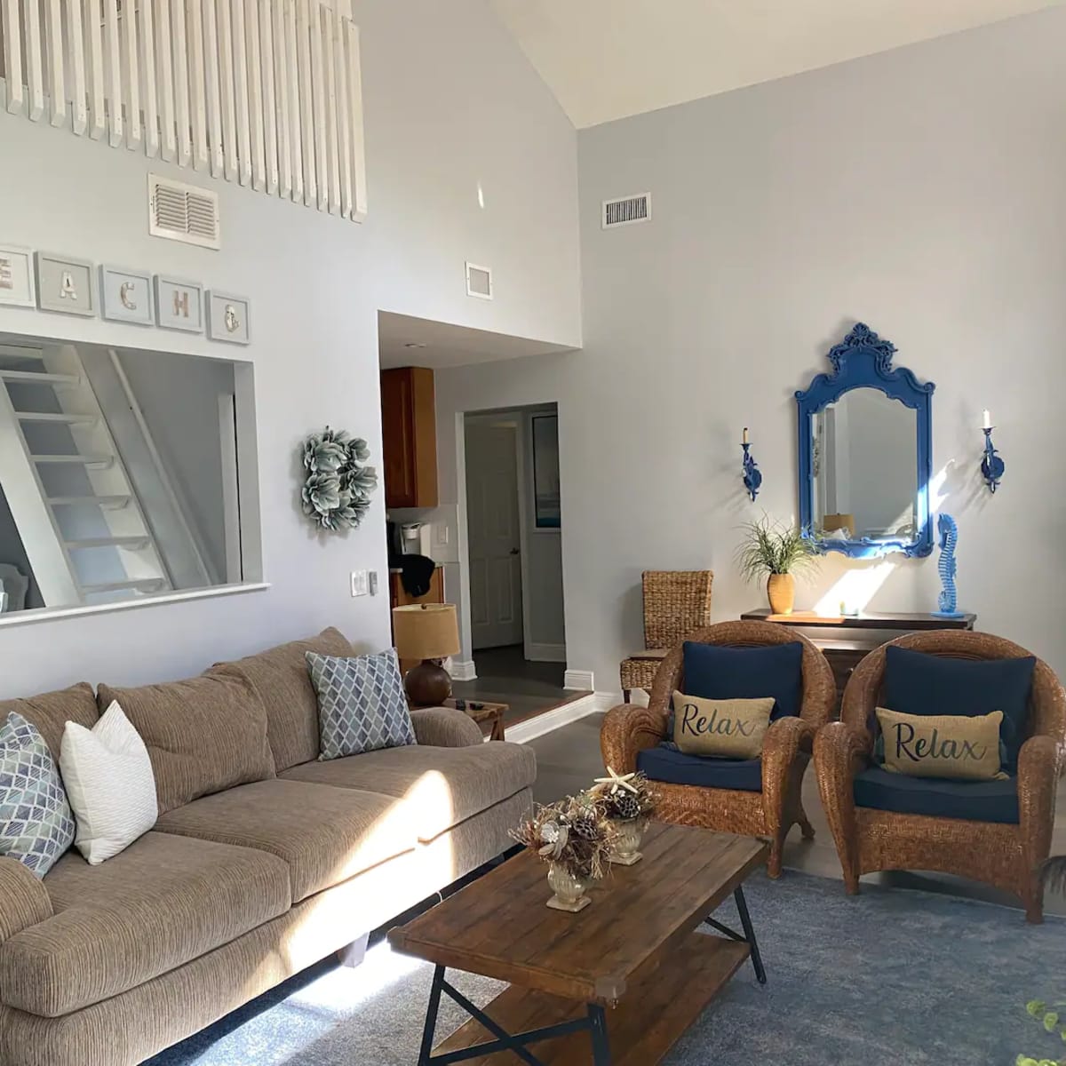 A spacious living room features a brown sofa, two blue accent chairs, a wooden coffee table, and a decorative mirror on the wall.