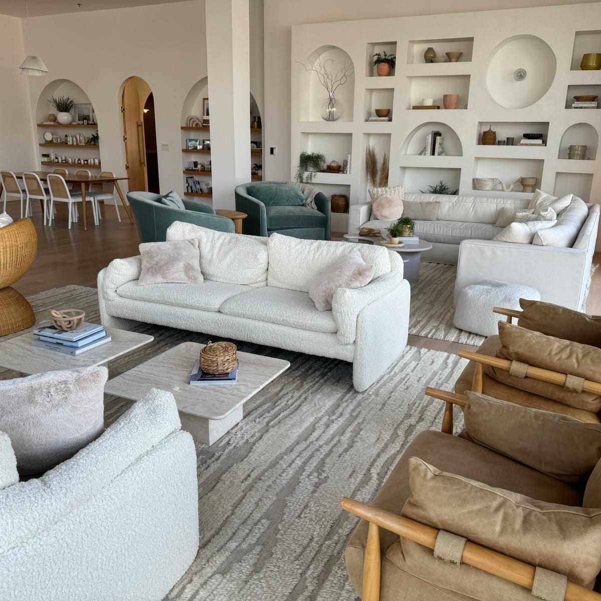 A spacious living room with multiple seating arrangements, including plush sofas and armchairs, and shelves displaying decorative items.
