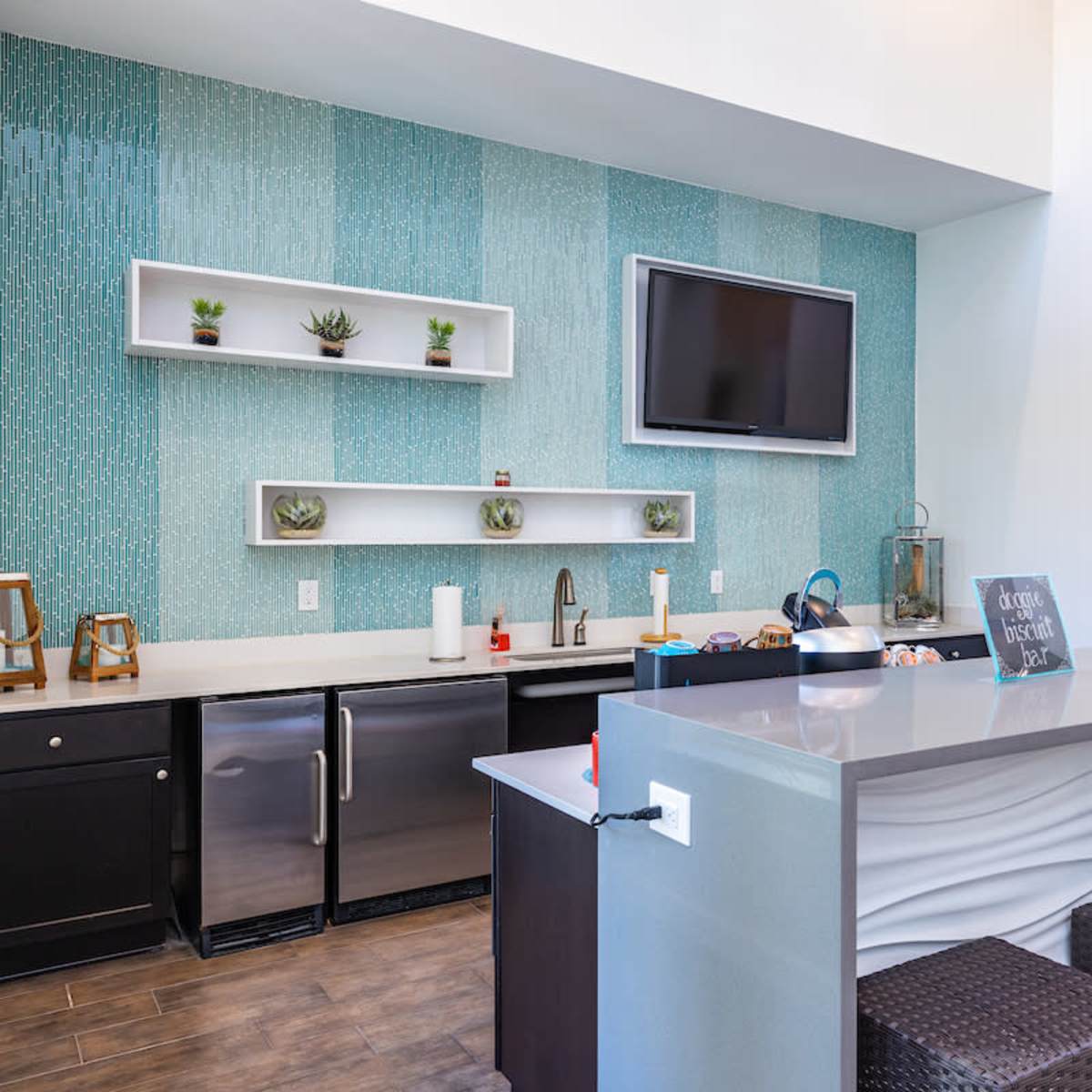 A modern kitchen with a light blue accent wall, stainless steel appliances, and a gray island with woven stools.
