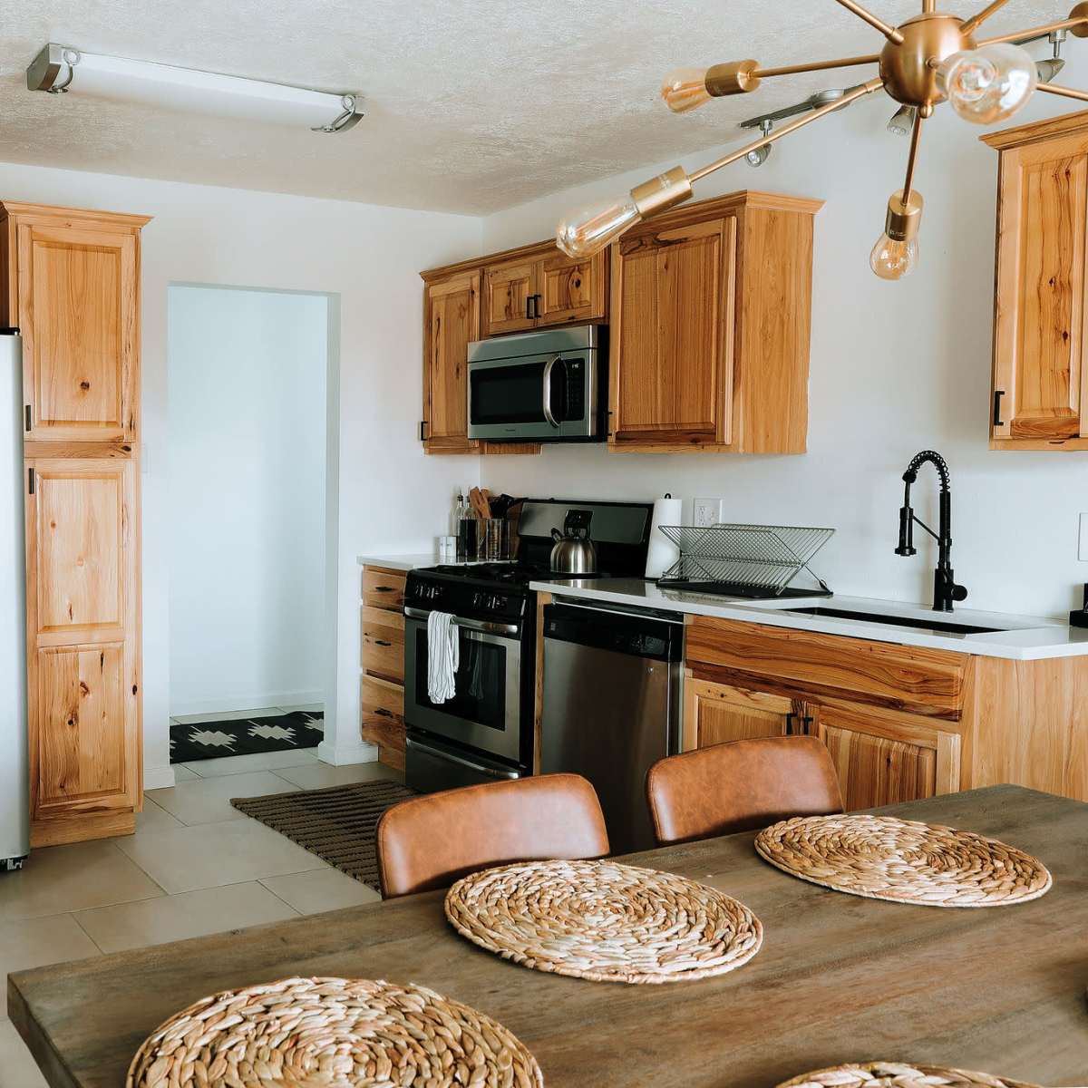 A modern kitchen with wooden cabinetry, stainless steel appliances, and a dining table set with woven placemats.