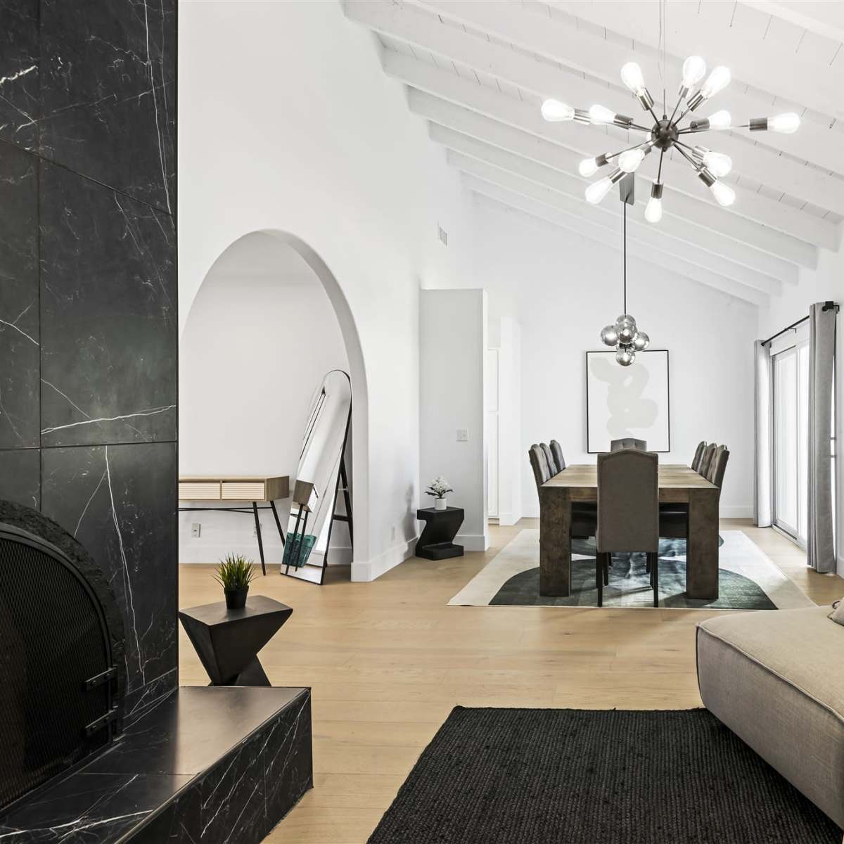 A modern, open-plan living space featuring a minimalist sofa, a dining area with a long table, and vaulted ceilings with a statement light fixture.