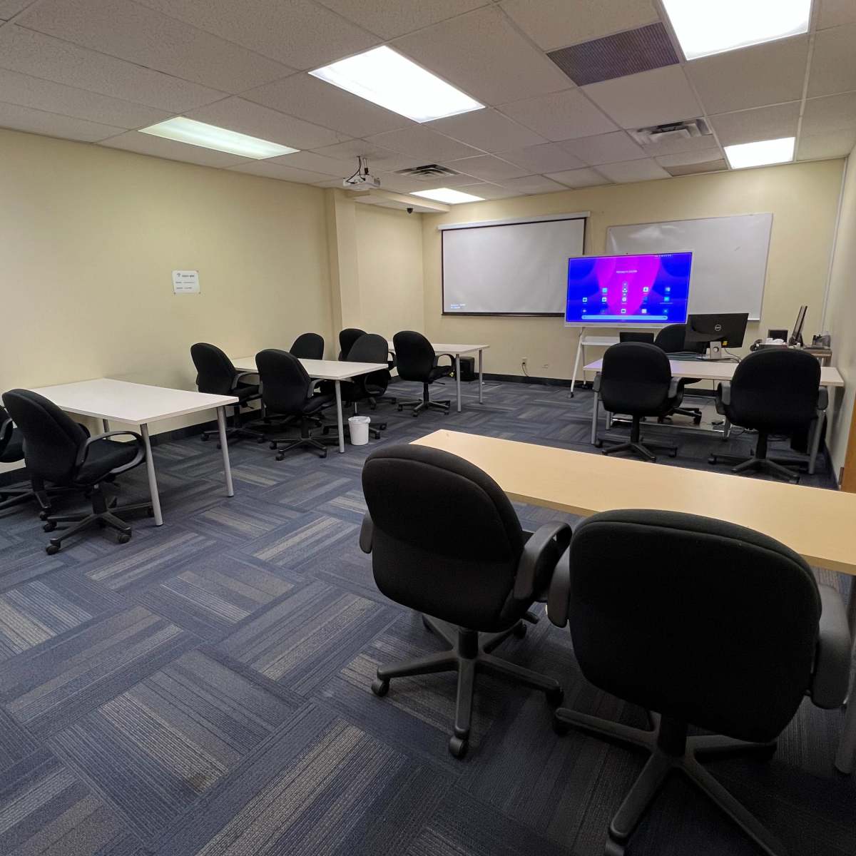 A conference room features several tables and chairs arranged around a presentation screen.