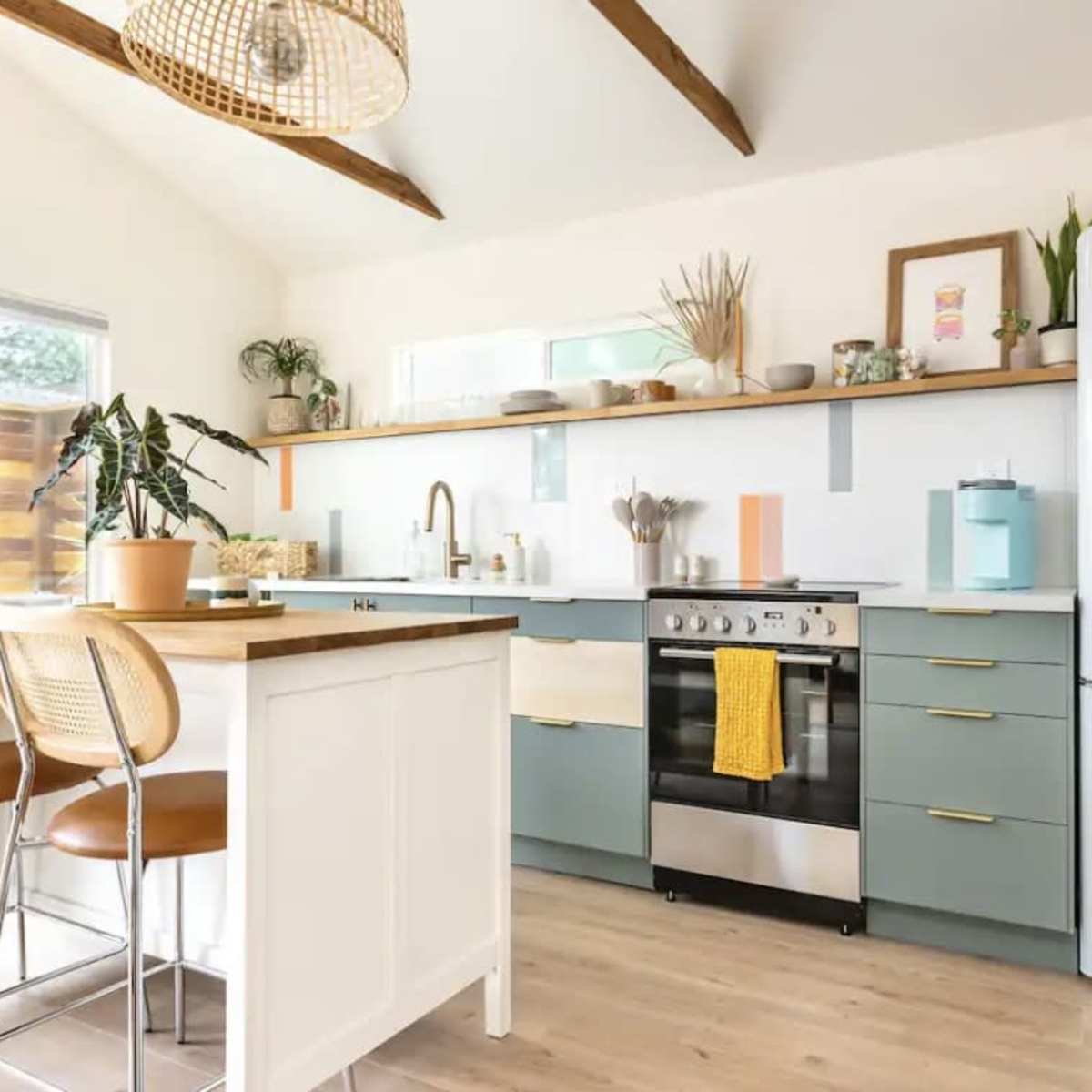 A modern kitchen features a central island, stainless steel appliances, and light wood accents with green cabinetry.