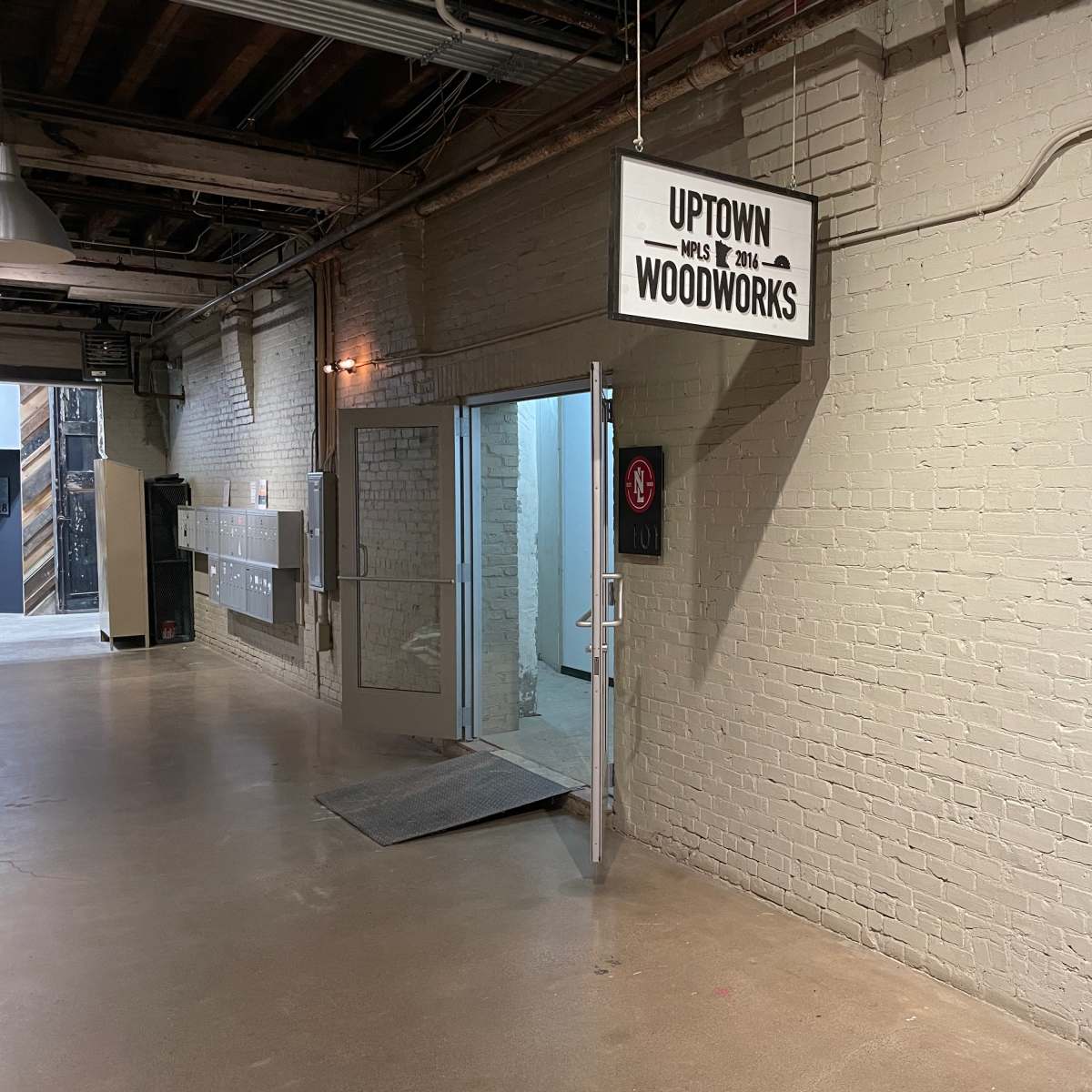 A hallway with a sign that reads "Uptown Woodworks" above an open door leading to a workshop area.