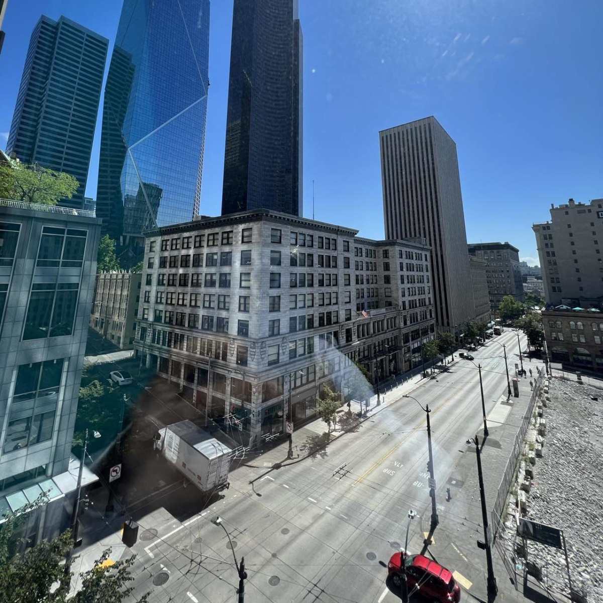 A cityscape with several high-rise buildings under a clear blue sky, viewed from a window overlooking a vacant street.