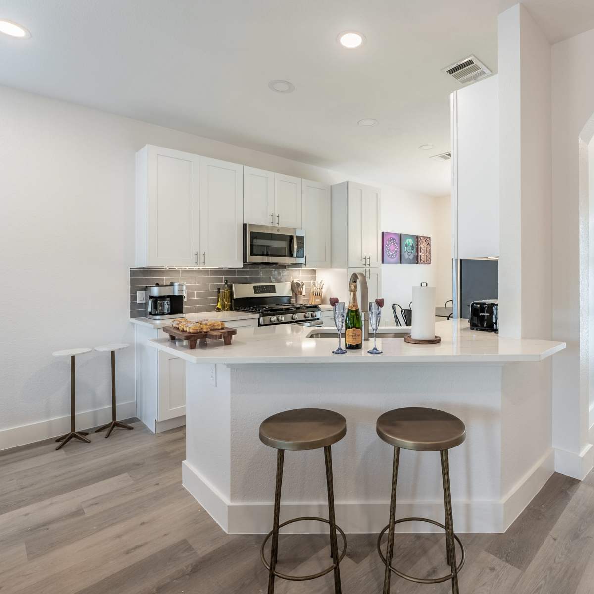 A modern kitchen features white cabinetry, stainless steel appliances, a central island with two stools, and a front door with glass panels.
