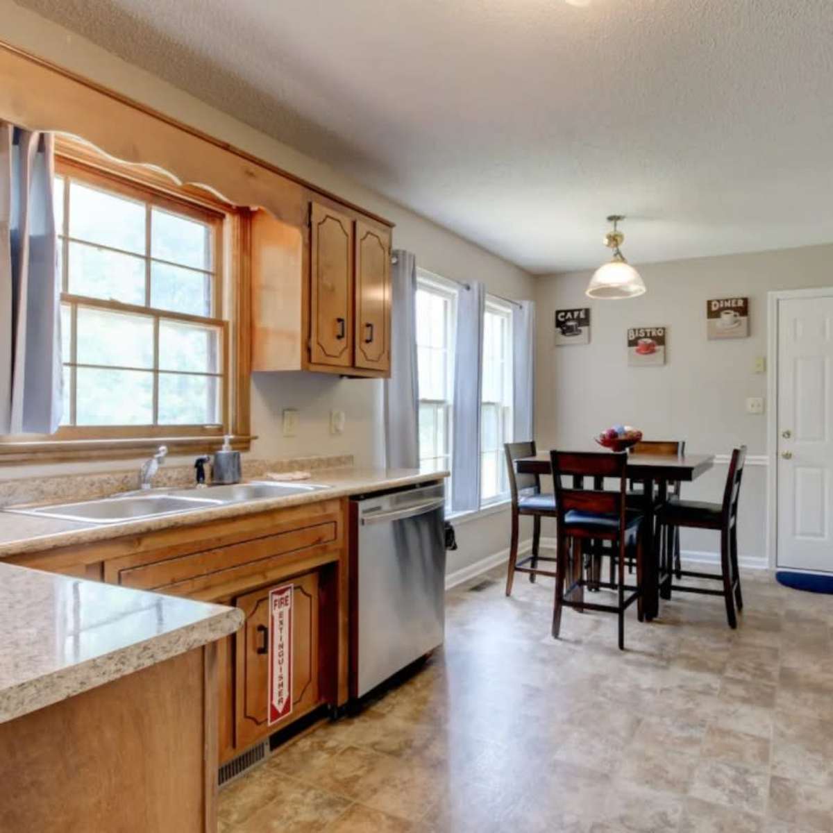 A tidy kitchen with wooden cabinets, a stainless steel dishwasher, and a small dining table with four chairs near a window.