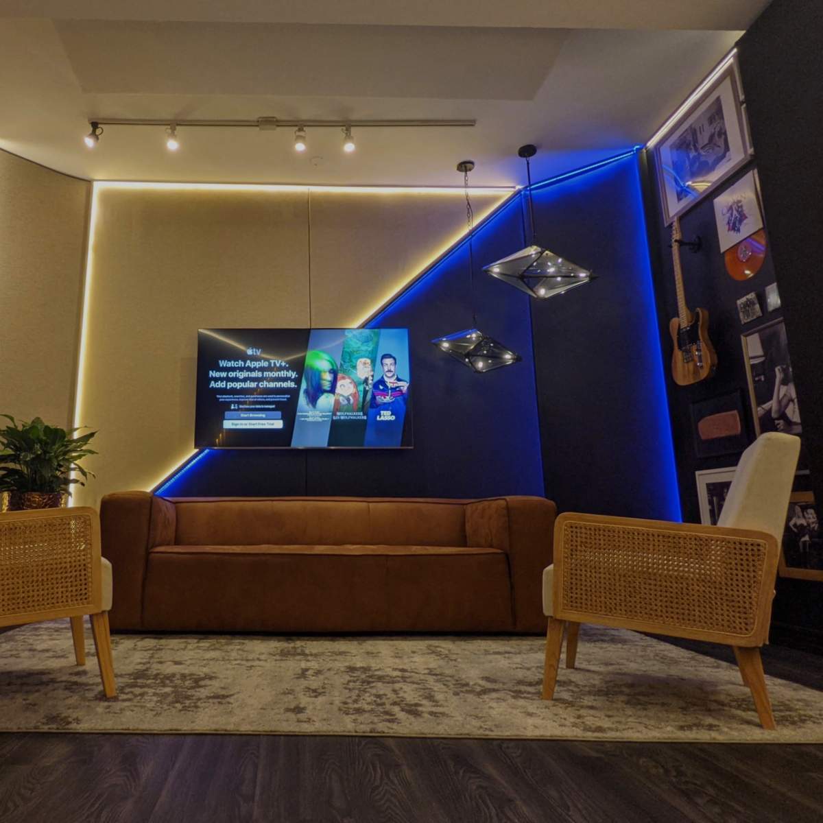 A modern living room features a brown couch, two wicker chairs, a wall-mounted television, and LED lighting accents.