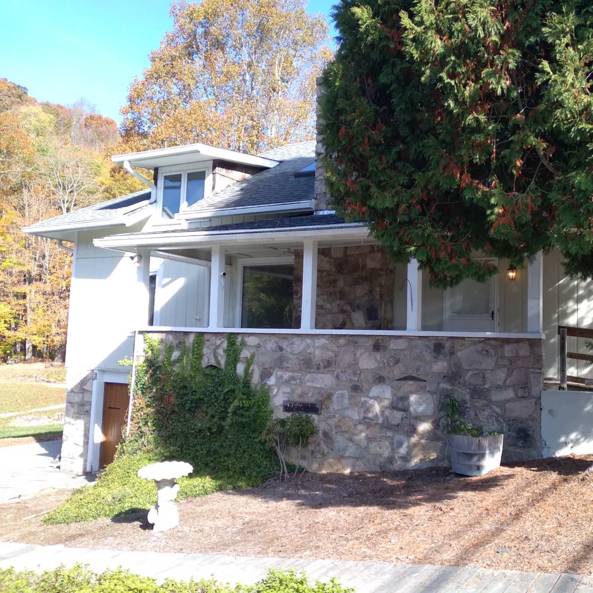 A house with a stone exterior and a large tree in front is surrounded by gravel pathways and landscaping.