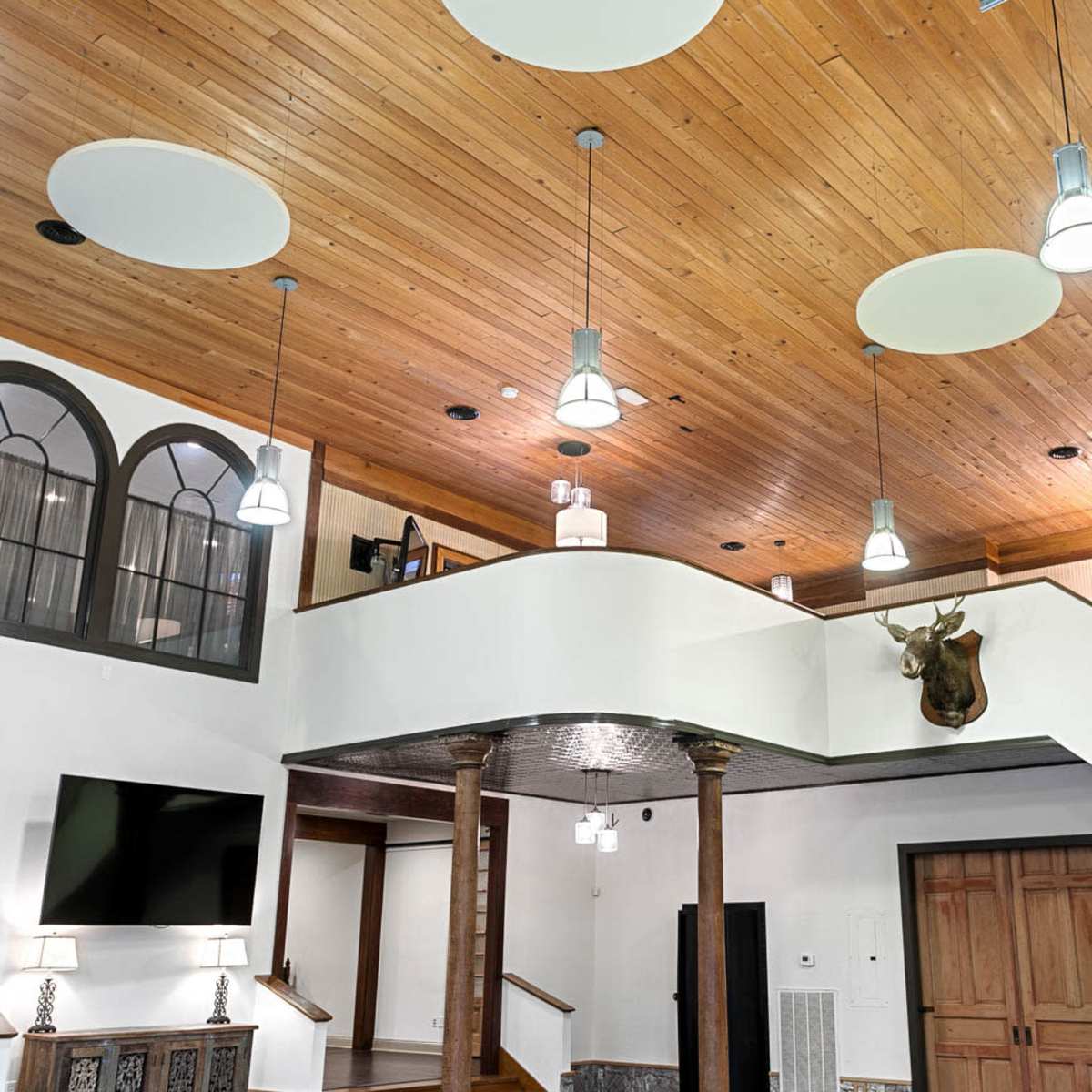 A spacious interior with a wooden ceiling, modern light fixtures, and a staircase leading to an upper level.