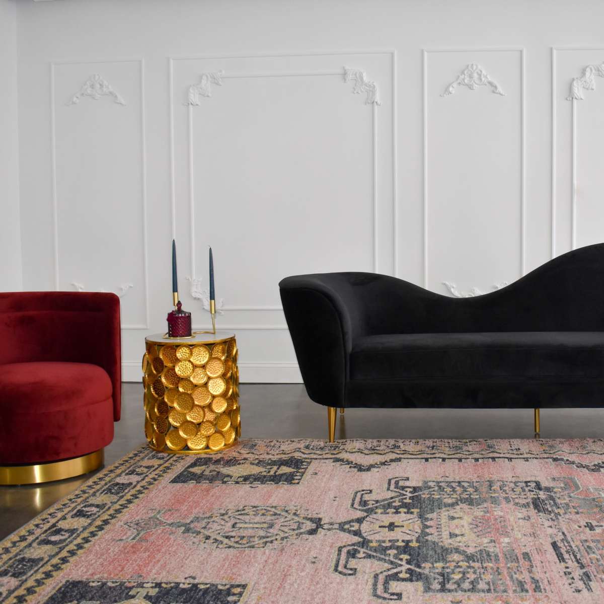 A modern seating arrangement with a red armchair, a black couch, and a gold-accented side table on a patterned rug in a minimalist setting.