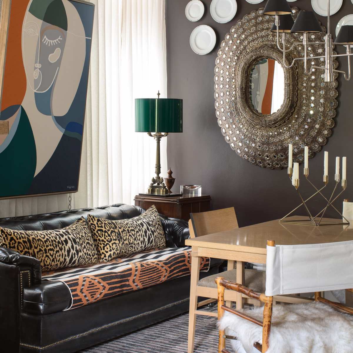 A stylish dining area featuring a black leather sofa adorned with animal print pillows, a wooden dining table surrounded by chairs, and decorative plates displayed on a dark wall.