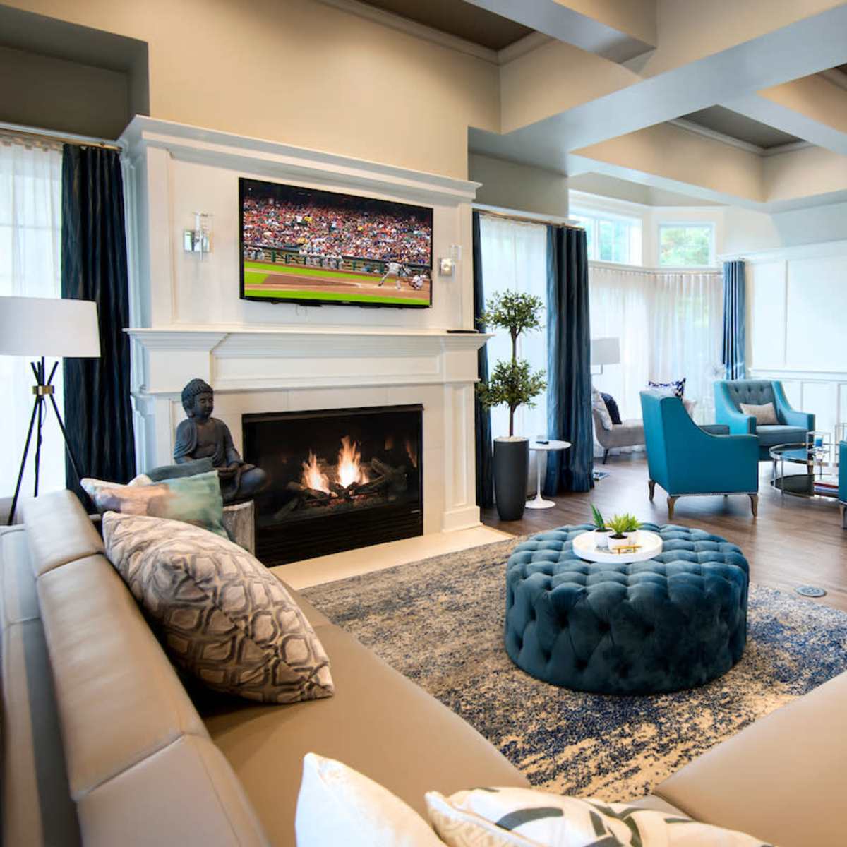 The living room features a modern design with a fireplace, large windows, and two televisions displaying a sports event.