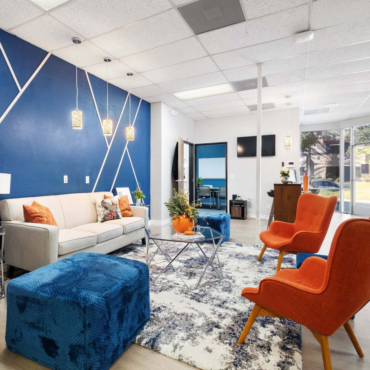A modern interior space with a light sofa, orange armchairs, a blue ottoman, and a geometric blue accent wall.