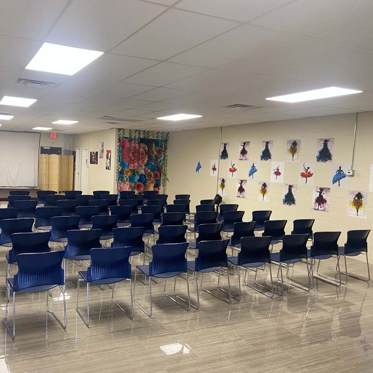 A spacious, empty meeting room arranged with rows of blue chairs facing a presentation area at the front.