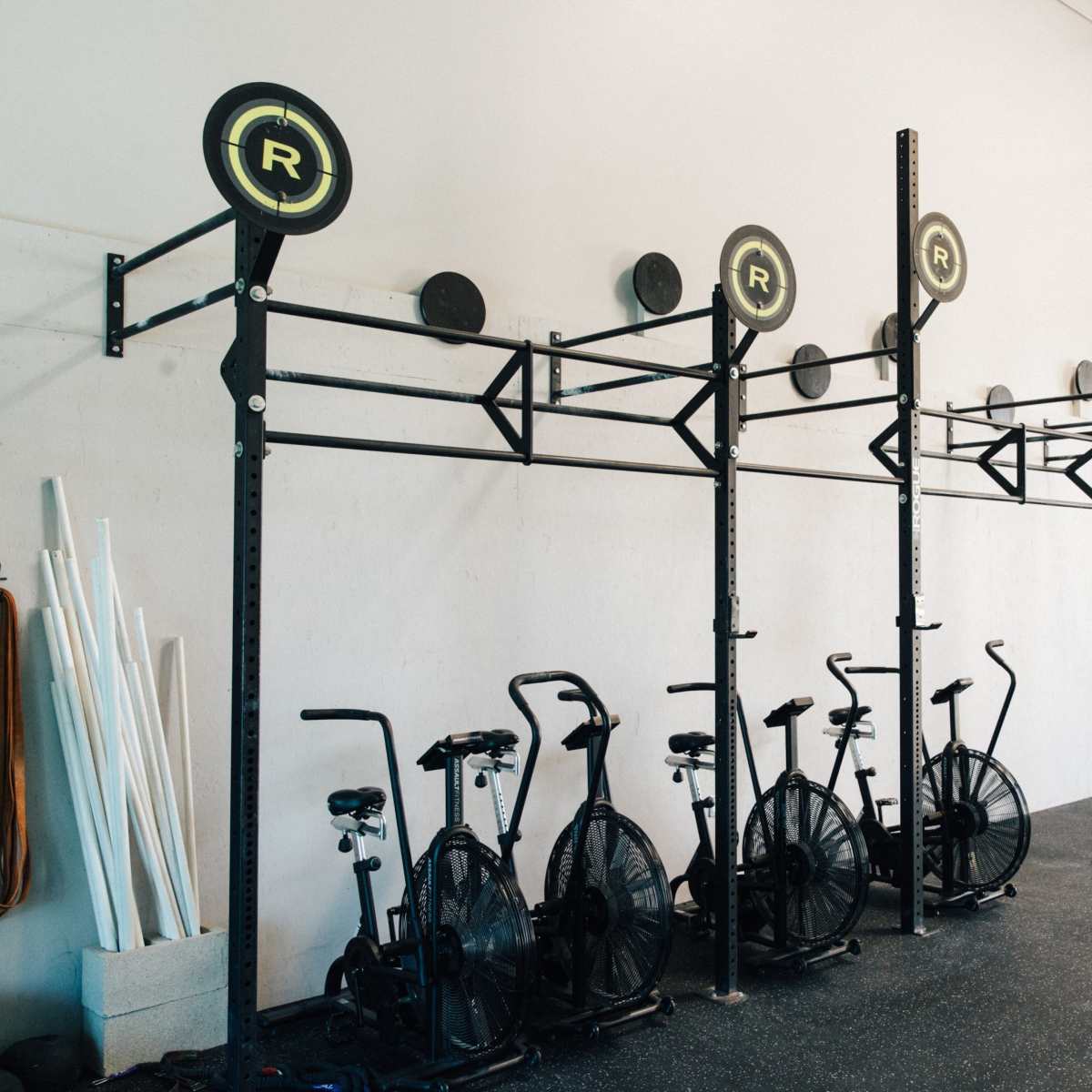 A fitness studio with black exercise bikes lined up against a wall, alongside vertical bars and gym equipment.
