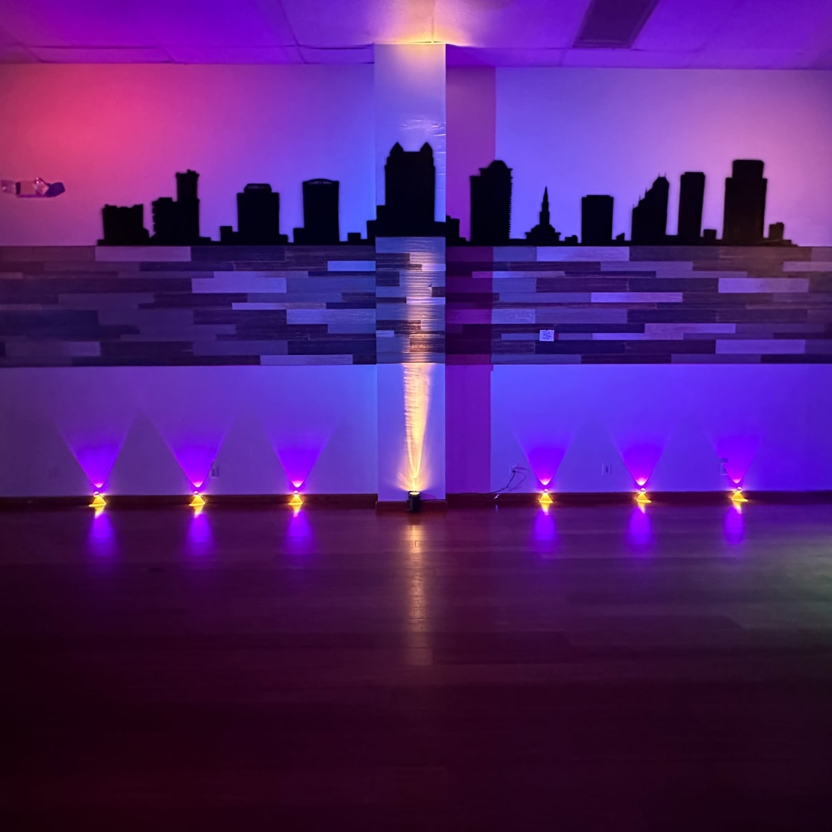 A dimly lit room featuring a silhouette of a city skyline against a wall with purple and yellow lighting.