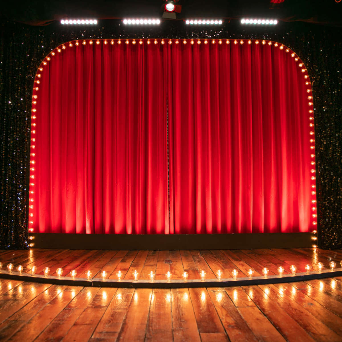 A stage with red velvet curtains, framed by lights, set on a wooden floor.