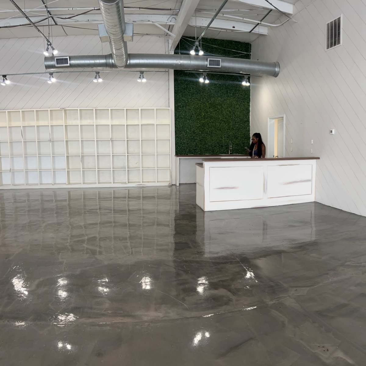 An open interior space features a polished concrete floor, white walls with vertical paneling, and a reception area with a desk.