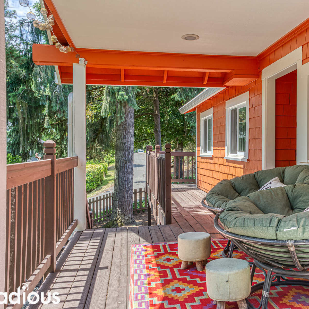 A porch with an oversized round chair, a colorful patterned rug, and an orange accent wall.